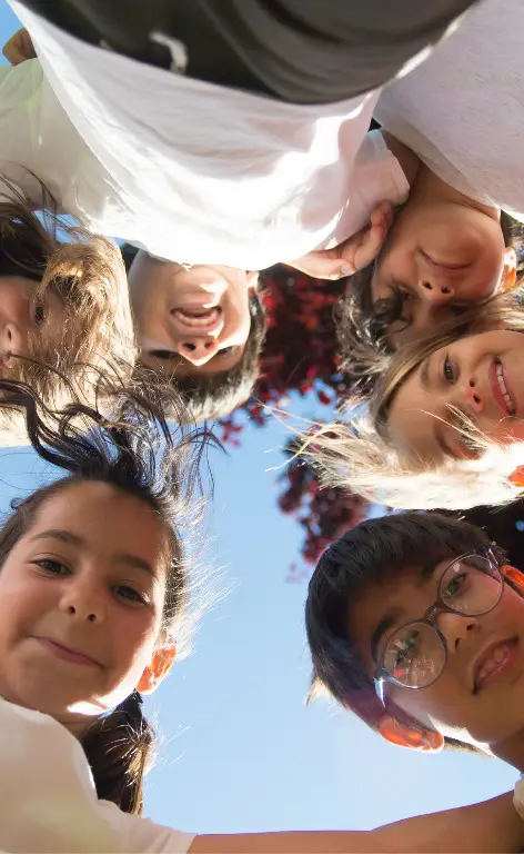 Children in a circle, arms around each other's shoulders, smiling down at the camera