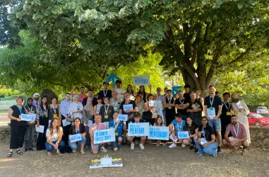 Foto grupal al aire libre de muchas personas sonriendo y mostrando carteles que dicen "Yo confío en los jóvenes" y "¡Viva mi mentora!"