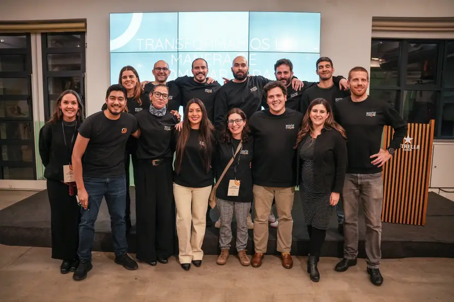Foto de grupo del equipo de Worldcoo: personal de pie y sonriendo frente a una pantalla de presentación en la oficina