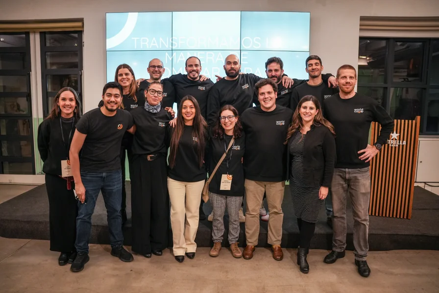 Foto de grupo del equipo de Worldcoo: personal de pie y sonriendo frente a una pantalla de presentación en la oficina